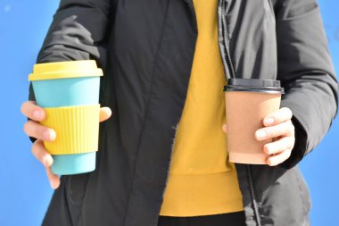 İki elinde de eko kahve fincanı tutan bir kadın, biri plastik kapaklı tek kullanımlık karton bardak, diğeri ise yeniden kullanılabilir bambu bardak. Sürdürülebilir yaşam tarzı konsepti. Plastiğe hayır de.