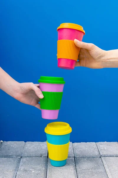 hands of two girls taking eco coffee cup on blue background, 