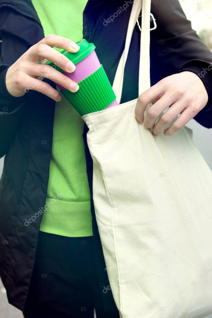Female hands holding reusable coffee cup putting into a bag outdoors.