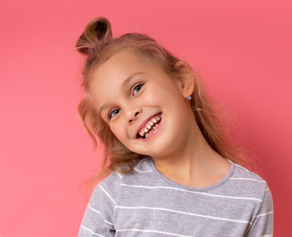 Funny little girl with a funny hairstyle standing smiling on a pink background