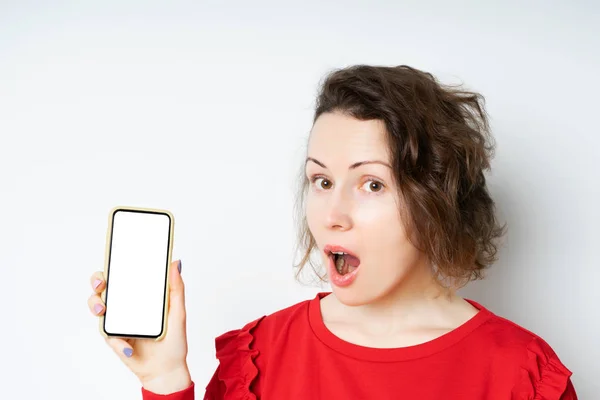 Retrato si una joven impactada en un suéter rojo mirando el teléfono móvil aislado — Foto de Stock