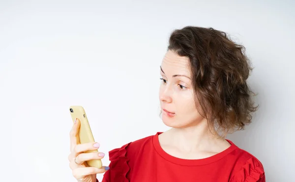Retrato si una joven impactada en un suéter rojo mirando el teléfono móvil aislado — Foto de Stock