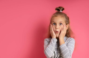 Bun saç stili, gri çizgili bluz giymiş küçük sarışın manken. Pembe arka planda poz verirken merak ediyor.