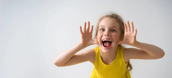 Menina pré-escolar feliz Sly em vestido amarelo ensolarado provocando alguém, gritando e rindo com um rosto engraçado. Close up estúdio tiro isolado em branco — Fotografia de Stock