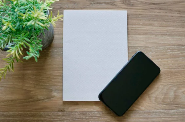 Λευκό χαρτί με smart phone με μικρά φυτά στο γκρι βάζο στο ξύλινο τραπέζι — Φωτογραφία Αρχείου