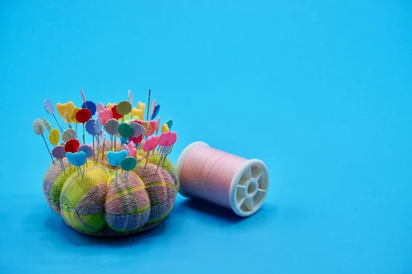 Hilo rosa con almohadilla de colores, alfileres y aguja de coser en el fondo azul — Foto de Stock