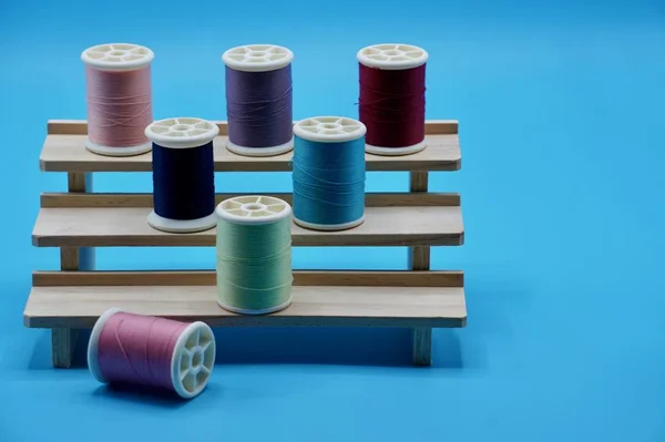 A group of pink, purple, blue, green and red thread on the wooden stand on the blue background — Stock Photo, Image