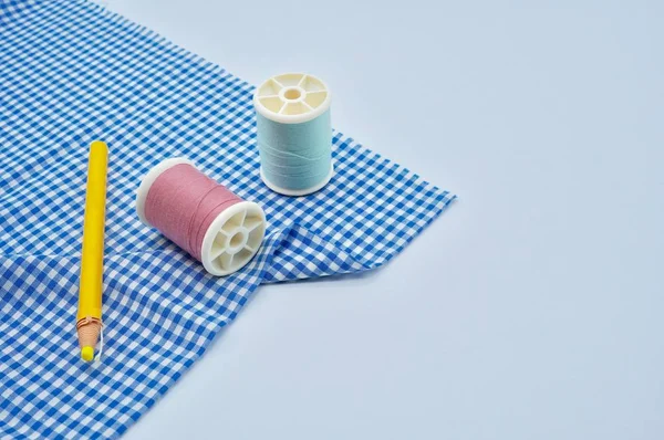 Hilos rosados y verdes, lápiz de tela amarilla con tela azul sobre fondo blanco — Foto de Stock