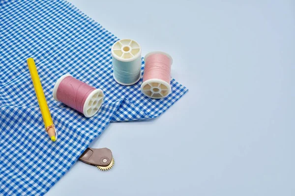 Pink and green threads, yellow fabric pencil, sewing tracing wheel with blue checked fabric on the white background — Stock Photo, Image