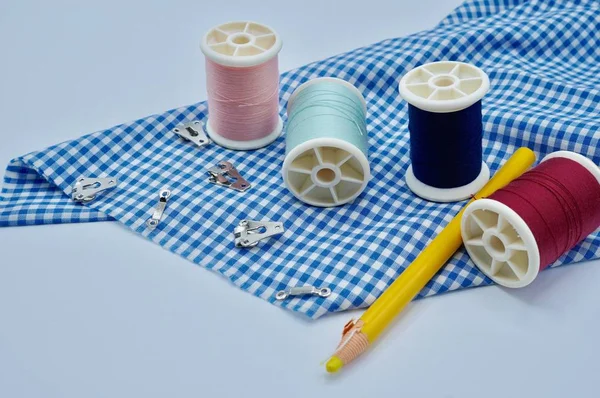 Hilo rojo, rosa, azul y verde con ganchos de falda y ojos con lápiz amarillo en la tela a cuadros azul sobre el fondo blanco — Foto de Stock