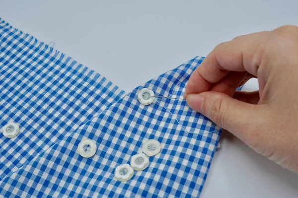 Mano con aguja de coser unida un botón a la tela azul sobre el fondo blanco — Foto de Stock