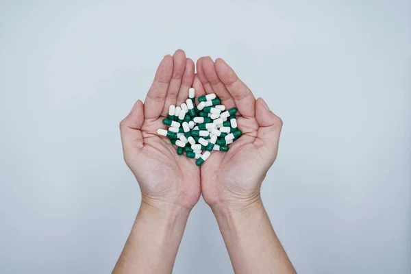 Hands holding a lot of white and green capsules on the gray background — Stock Photo, Image