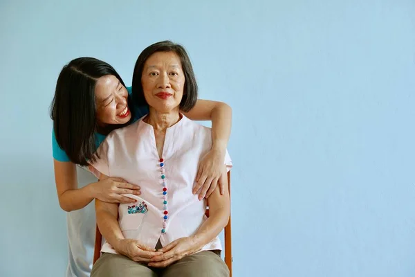 Una madre asiática en blusa rosa y una hija asiática en blusa azul en una habitación azul — Foto de Stock