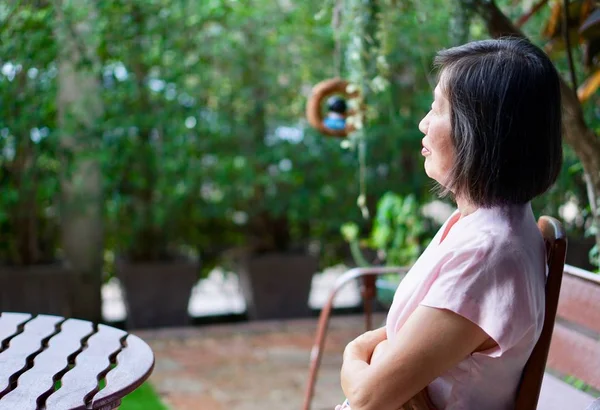 Una vieja mujer asiática en blusa rosa sentada en la silla en el jardín — Foto de Stock