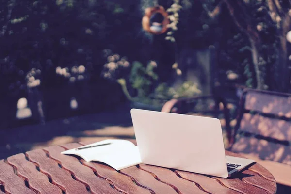 Un libro de computadora, bolígrafo y diario sobre la mesa de madera en el jardín en el día soleado —  Fotos de Stock