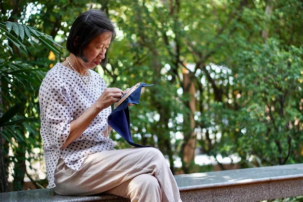 An old asian woman sitting on the bench embroidering handkerchief in the garden