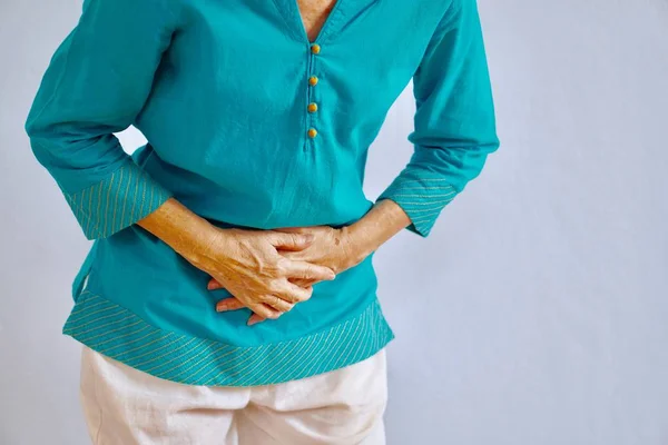 A woman in blue blouse standing in front of gray background getting belly pain — 图库照片