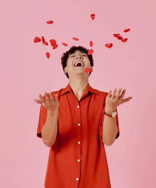 Een jonge Aziatische man met vrolijke glimlach gezicht en in rood shirt gooien rode hart vormen, roze achtergrond — Stockfoto