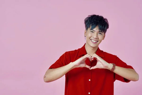 A man in red shirt holding two hands as a heart shape sign standing on the pink background — Stok fotoğraf