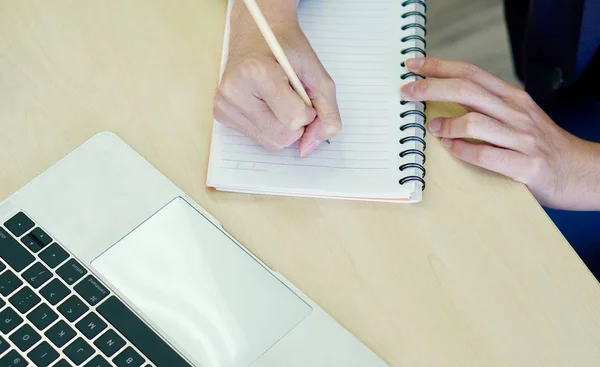 Un hombre de negocios escribiendo en un cuaderno al lado de la computadora en la mesa de madera — Foto de Stock