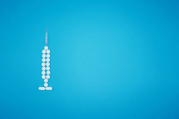 Bílé pilulky předstírají, že jsou stříkačkou na modrém pozadí — Stock fotografie