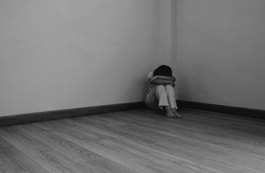 A young sad woman with depressive mood sitting in the corner of the room. black and white tone