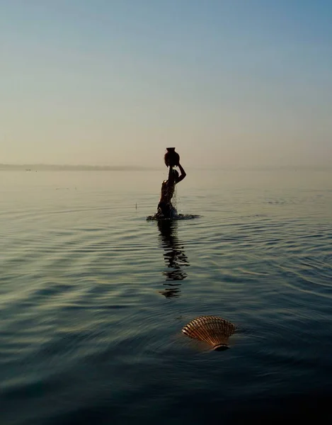 Silhouette of a boy holding a bamboo jar above the head, standing in the water at sunrise — Stockfoto