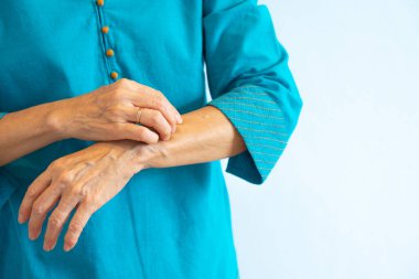 Mavi bluzlu yaşlı bir Asyalı kadın kaşınıyor.