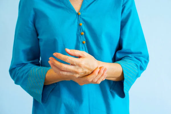 Een oude vrouw in blauwe blouse krijgt pols gewrichtspijn, grijze rug — Stockfoto