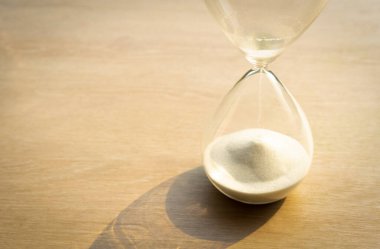 Tahta masanın üzerinde beyaz kum olan bir kum saati zamanı temsil eder.