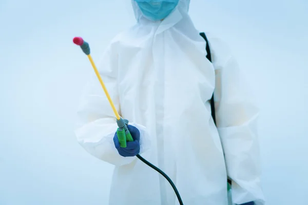 worker in personal protective equipment including white suit mask and face shield sparaying disinfectant to control coronavirus infection (focus at hand)