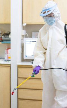 Beyaz giysi maskesi ve yüz kalkanı da dahil olmak üzere kişisel koruyucu ekipman işçisi. Coronavirüs enfeksiyonunu kontrol etmek için dezenfektan kullanıyor.