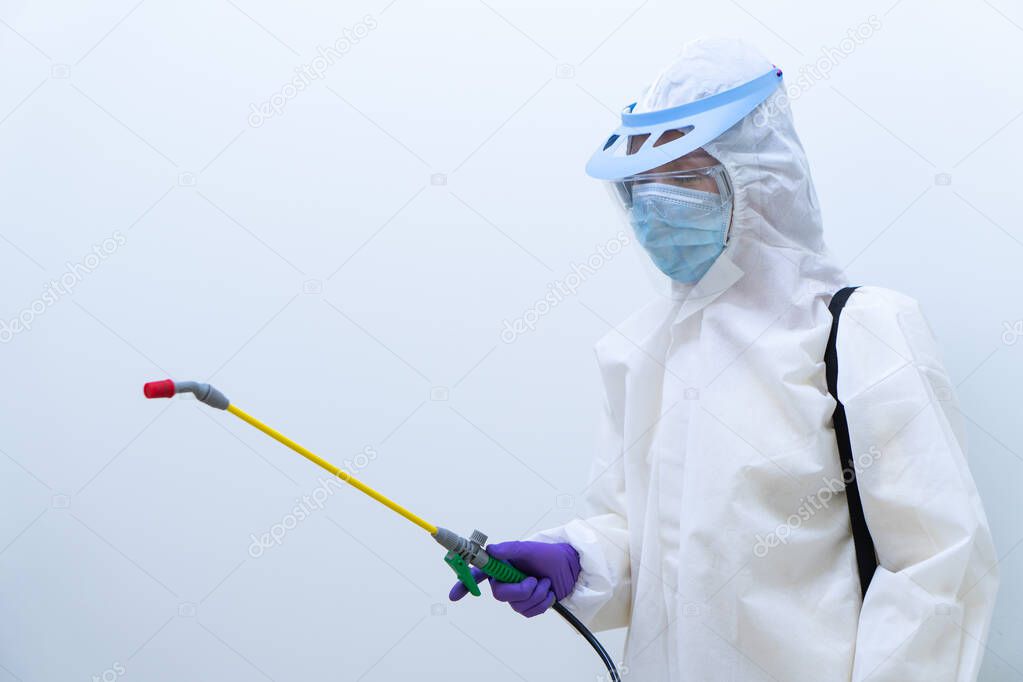worker in personal protective equipment including white suit mask and face shield sparaying disinfectant to control coronavirus infection (focus at hand)