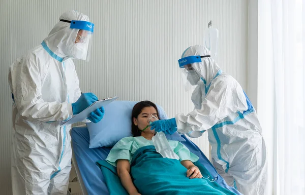 Kişisel koruyucu ekipmandaki doktorlar ya da salgın sırasında hastanede karantina altında olan Asyalı kadın hastaya oksijen maskesi ve koronavirüs enfeksiyonu veren doktorlar. tıbbi konsept