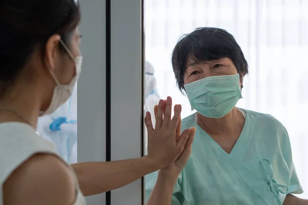 マスクをしたアジア系の娘は 19歳の時に感染した母親や 入院中の隔離室で隔離されたコロナウイルスに感染した母親を訪ねます 家族関係の概念 — ストック写真