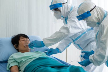 Doktor ve hemşire kişisel koruyucu ekipmanlarda ya da Asyalı kadın hastaya salgın sırasında izolasyon ünitesinde kovid-19 ya da koronavirüs enfeksiyonu olan oksijen kanülü veriyor. tıbbi konsept