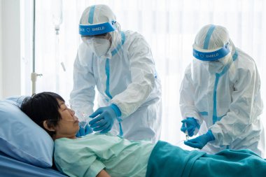 Korunma ekipmanındaki doktorlar ya da salgın sırasında hastanede karantina altında olan Asyalı kadın hastaya oksijen maskesi ya da koronavirüs enfeksiyonu veren doktorlar. tıbbi konsept