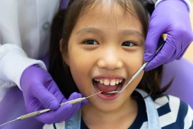 Dişçi, Asyalı çocuğun dişlerini temizlemek ve klinikteki diş çürüklerini tedavi etmek için dişçi aletleri kullanıyor. Diş hekimliği ve sağlık hizmeti kavramı