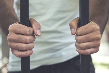 Genç adam parmaklıkları tutuyor.