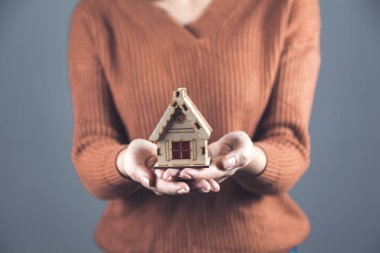 Kadın ev modelini gri duvar arkasında tutuyor.