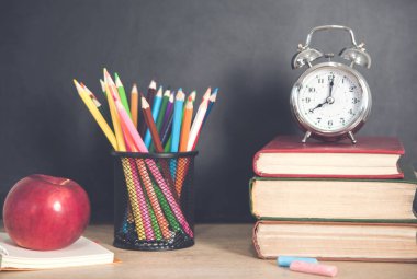  Kalemlerle kitap üzerinde saat ve karatahtanın üzerinde elma