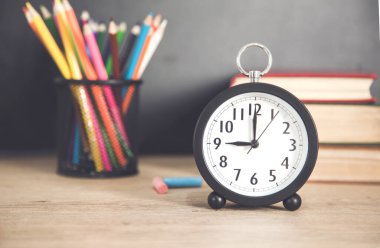 Masasında kitap olan saat ve renkli kalemler.