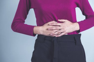 Gri duvar arkasında karın ağrısı çeken bir kadın.