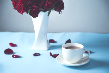 Masanın üzerinde kahve fincanları olan kırmızı güller.