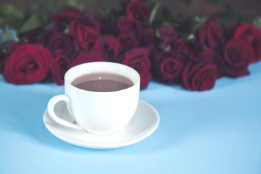 Masanın üzerinde kahve fincanları olan kırmızı güller.