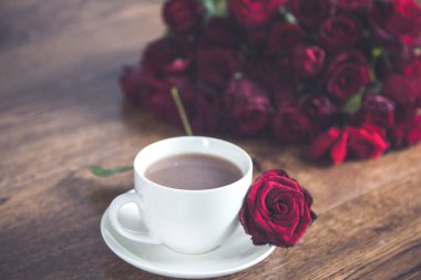 Masanın üzerinde kahve fincanları olan kırmızı güller.