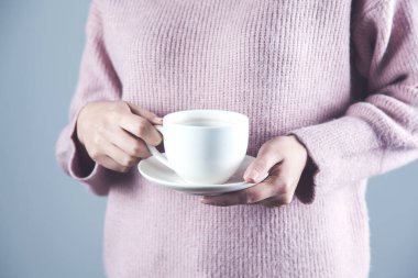 Bir fincan çay ya da kahve tutan bir kadın.