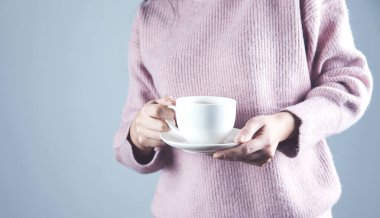 Bir fincan çay ya da kahve tutan bir kadın.