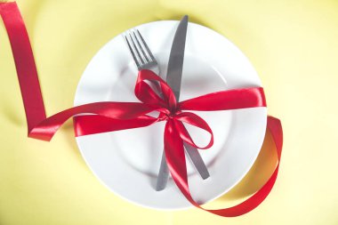 Masada kırmızı kurdeleyle bağlanmış kaşık, bıçak ve çatal.