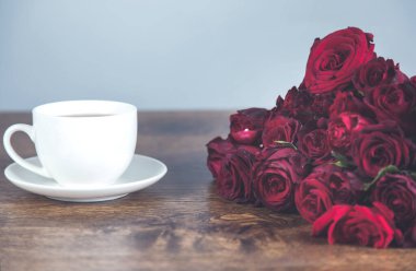 Masada bir fincan kahve ile kırmızı güller